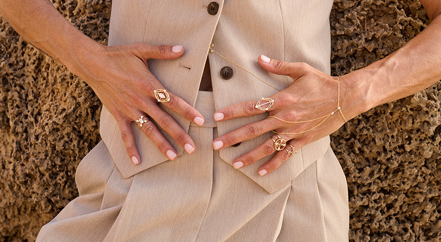 Hands wearing multiple ANNOORY gold rings and body chain jewelry